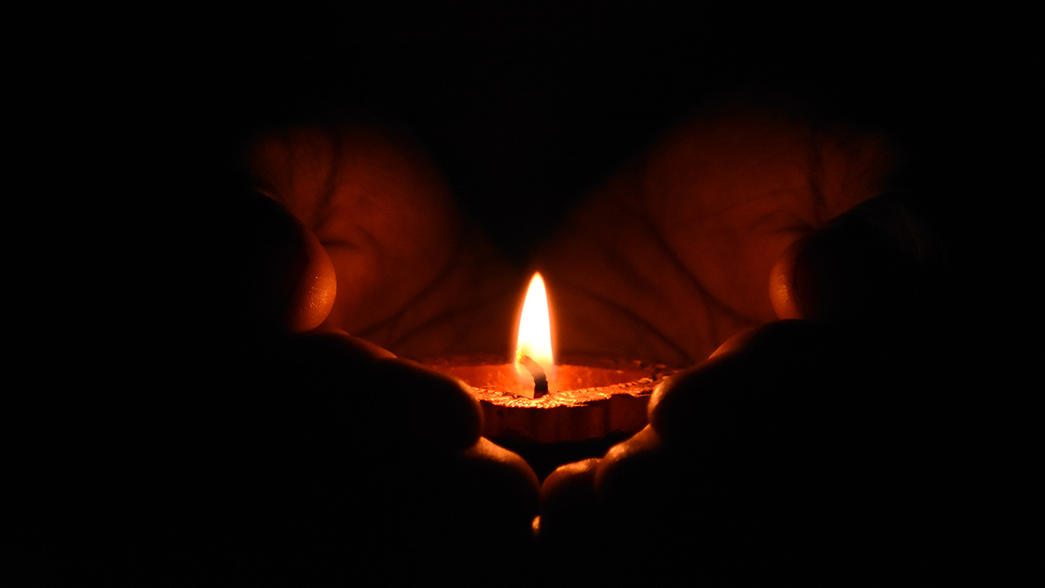 Two hands carrying a lit candle