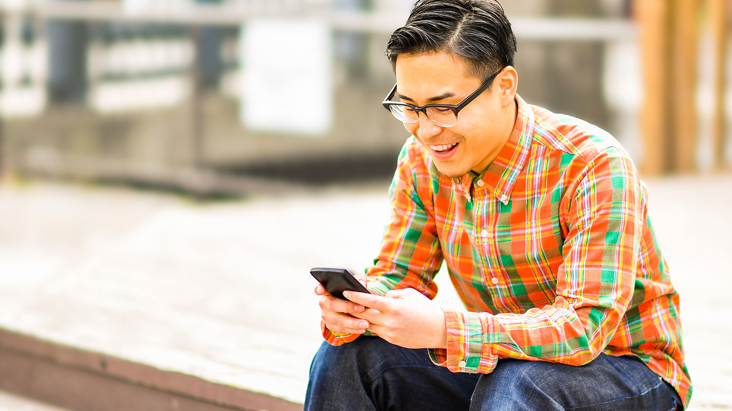 Asian faculty member sitting outside using phone