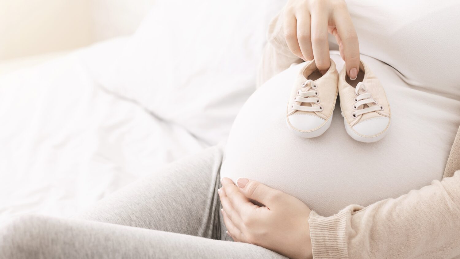 Pregnant person holding infant shoes over their pregnant belly