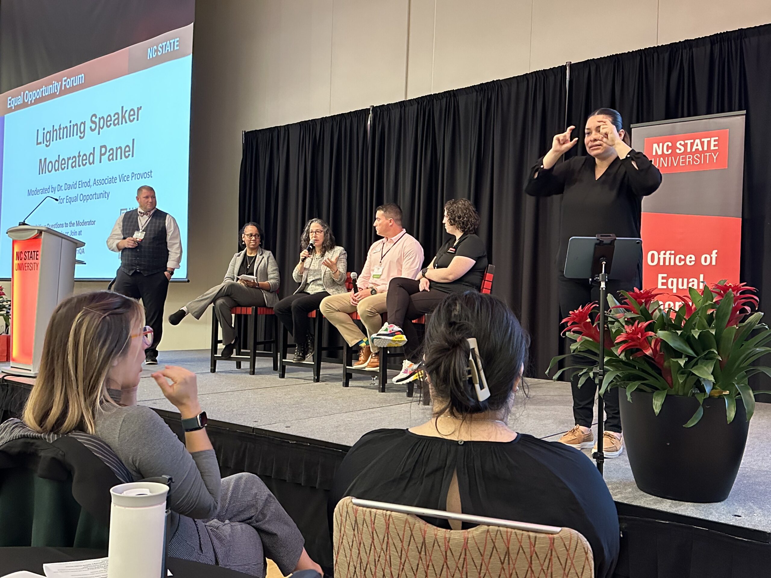 EO Forum - a panel of four speakers sitting on a state with a moderator asking questions. ASL interpreter standing to the right.